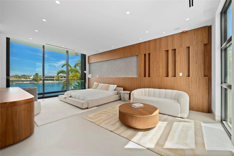 Expansive floor-to-ceiling windows, water frontage, wood-paneled accent wall, recessed lighting, and light-toned flooring