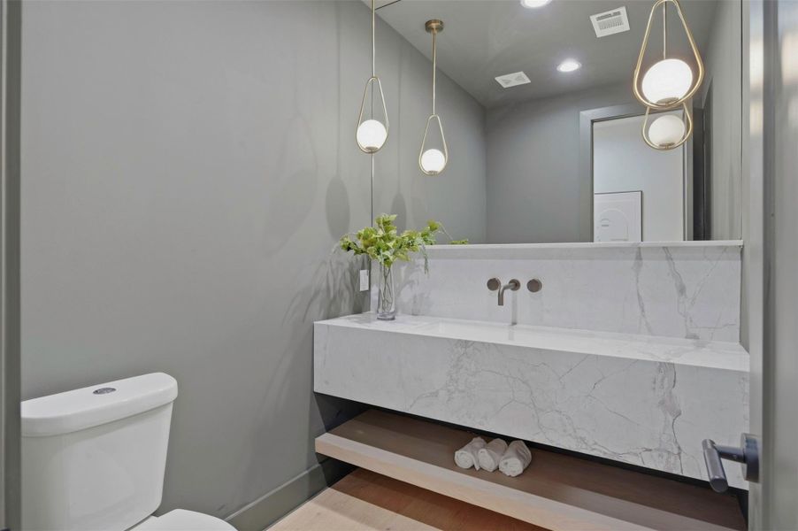 Statement powder bath features a custom floating 3 cm quartzite vanity, full-height glass mirror, and elegant chandeliers for a dramatic, elevated finish.