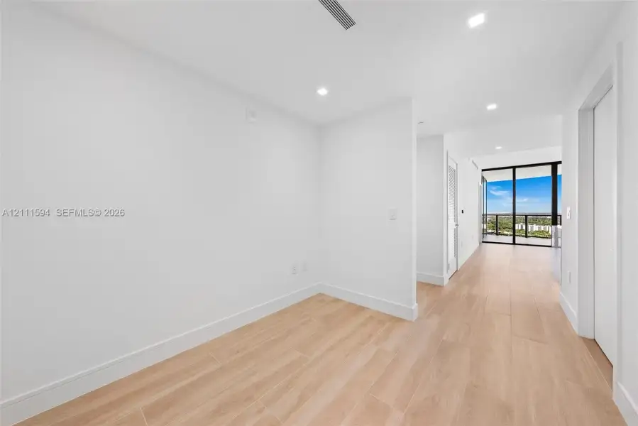 Interior space featuring light-toned wood-finish flooring, recessed ceiling lighting, and floor-to-ceiling glass sliding doors with balcony access Interior space featuring light-toned wood-finish flooring, recessed ceiling lighting, and floor-to-ceiling glass sliding doors with balcony access