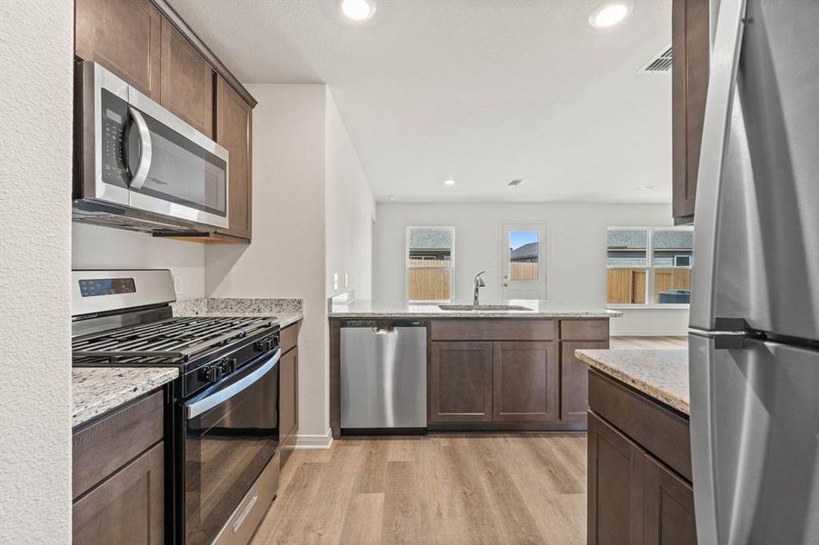 Kitchen featuring light stone countertops, dark brown cabinets, stainless steel appliances, light wood-type flooring, and sink