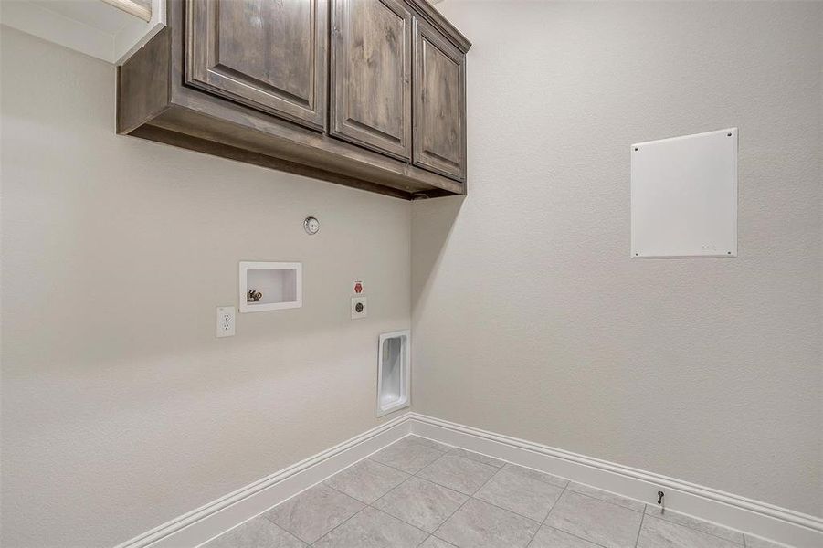 Clothes washing area with gas dryer hookup, hookup for an electric dryer, cabinets, hookup for a washing machine, and light tile patterned floors