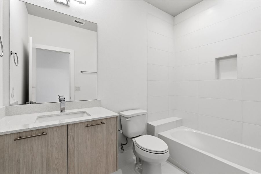 A well-appointed shared bath for the guest rooms, finished with clean-lined tile, a built-in shower niche, and practical storage that keeps the space feeling uncluttered.