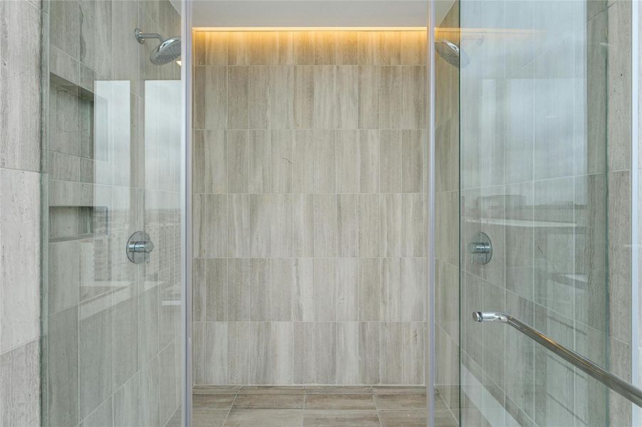 Expansive walk-in shower in the primary bathroom, wrapped in floor-to-ceiling stone tile with dual showerheads and sleek glass enclosure.