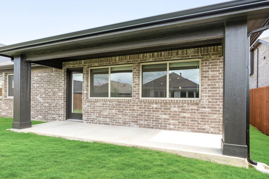 Covered back patio with concrete slab, brick exterior, large windows, and green lawn