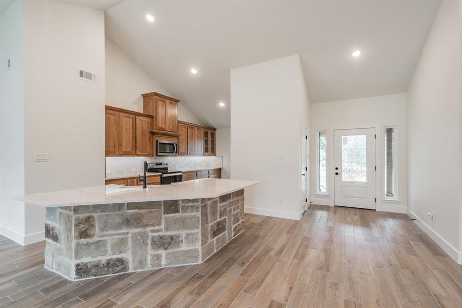 Kitchen featuring appliances with stainless steel finishes, brown cabinets, high vaulted ceiling, baseboards, and a spacious island