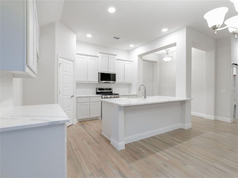 Kitchen with pendant lighting, sink, light stone countertops, appliances with stainless steel finishes, and white cabinetry