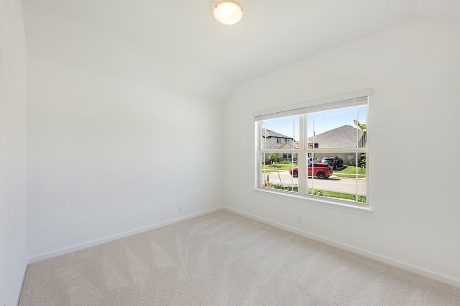 Empty bedroom with vaulted ceiling, beige carpet, and a window overlooking a neighborhood street Empty bedroom with vaulted ceiling, beige carpet, and a window overlooking a neighborhood street