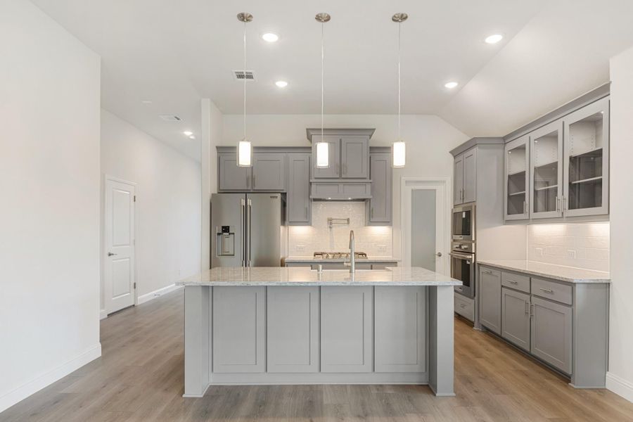 Kitchen with gray cabinets, large center island, granite countertops, and stainless steel appliances on wood floors Kitchen with gray cabinets, large center island, granite countertops, and stainless steel appliances on wood floors