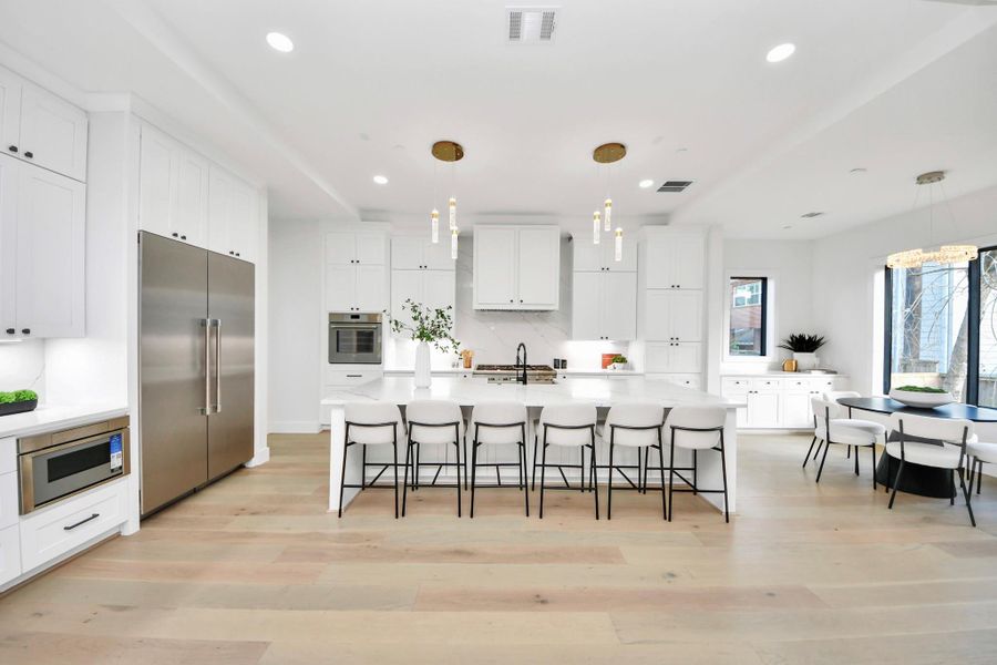 The kitchen showcases crisp white cabinetry, quartz countertops, and an impressive 11-foot island, all complemented by premium Thermador appliances and statement luxury lighting.