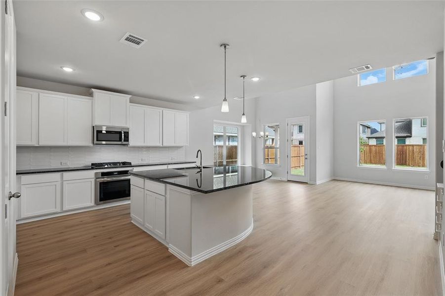 Kitchen featuring white cabinetry, backsplash, an island with sink, stainless steel appliances, and a high ceiling