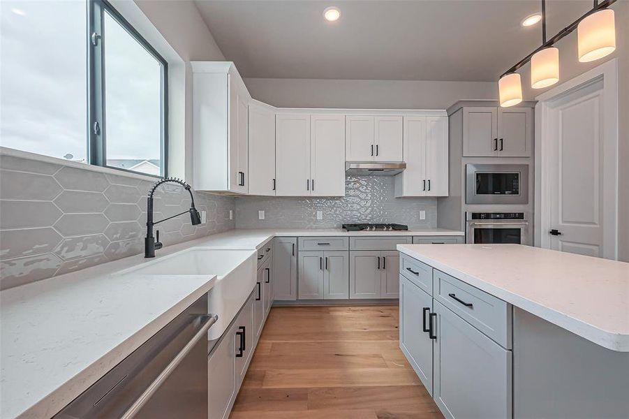 Discover this modern kitchen with sleek white cabinetry, a spacious island with stylish pendant lighting, and a farmhouse sink. The open design seamlessly connects to a bright living area, creating a welcoming and airy atmosphere.