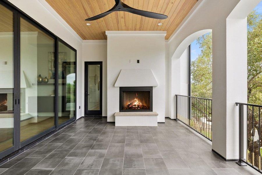 Covered outdoor living area featuring a wood-panel ceiling, dark tile flooring, and a built-in fireplace with a stone hearth