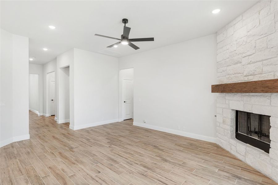 Open living room with stone fireplace, wood beam mantel, ceiling fan, and light wood-look tile floors