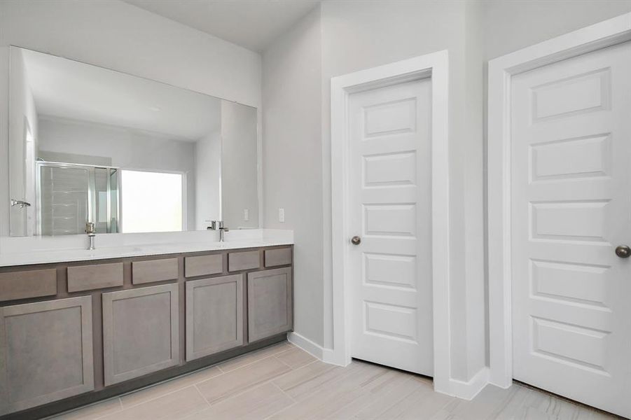 Light colored cabinets with light granite countertops complement the space, alongside a spacious walk-in closet with shelving, high ceilings, custom paint, and sleek, dark modern finishes. An ideal retreat for unwinding after a long day. Sample photo of completed home with similar floor plan. As-built interior colors and selections may vary.