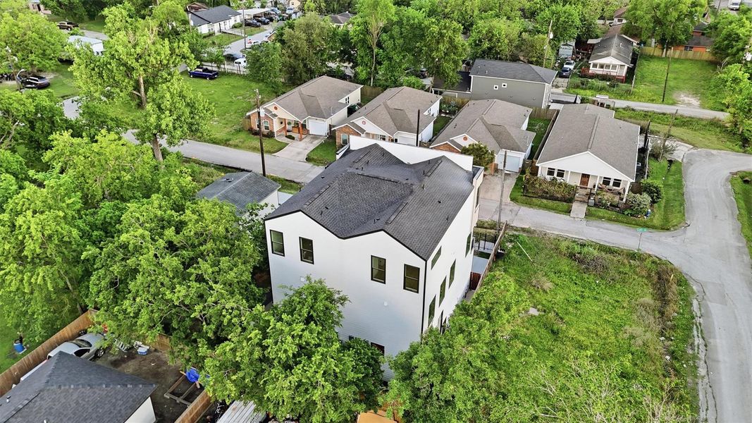 Elevated aerial view showcasing a modern three-story duplex nestled in an established neighborhood, surrounded by mature trees, nearby homes, and open green space—highlighting privacy, lot placement, and urban residential appeal.