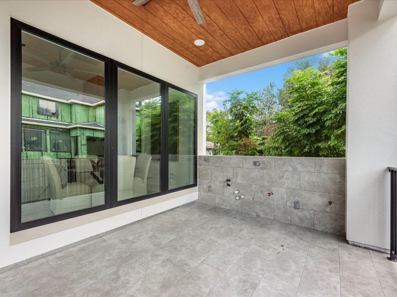 Outdoor kitchen pre-plumb, tiled upgraded flooring, designer wood paneling on the ceiling with a fan.