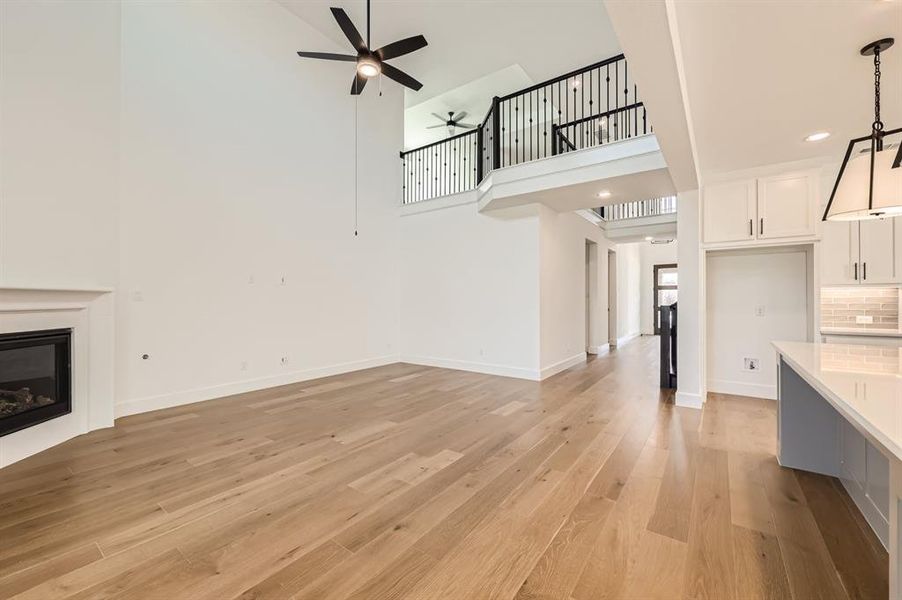 Unfurnished living room with a high ceiling, ceiling fan, and light hardwood / wood-style floors