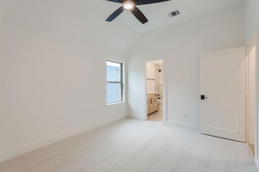 Unfurnished bedroom with connected bathroom, vaulted ceiling, ceiling fan, and light colored carpet