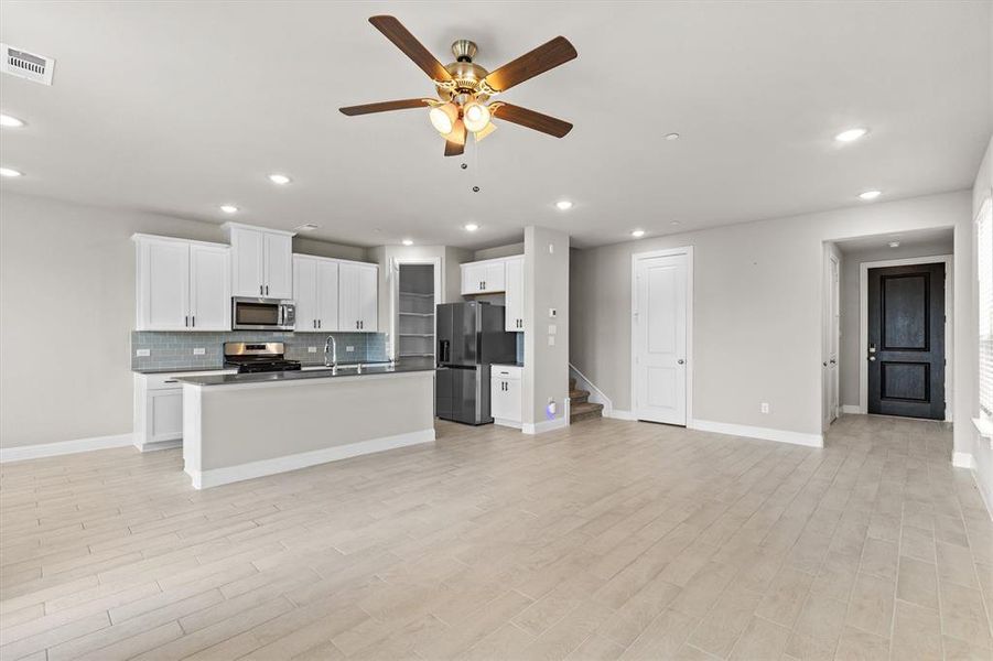 Kitchen with white cabinetry, light hardwood / wood-style flooring, an island with sink, ceiling fan, and appliances with stainless steel finishes