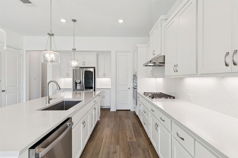 Kitchen with white cabinetry, stainless steel appliances, a kitchen island with sink, 5 burner gas cooktop, herringbone backsplash and pendant lighting Kitchen with white cabinetry, stainless steel appliances, a kitchen island with sink, 5 burner gas cooktop, herringbone backsplash and pendant lighting