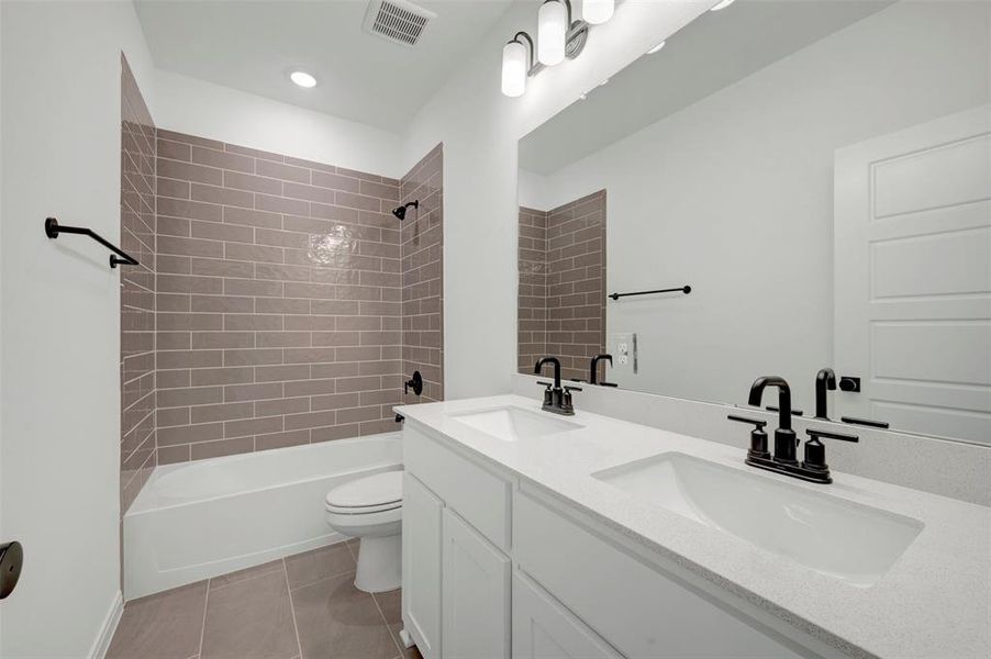 Bathroom featuring a double vanity with integrated sinks and matte black faucets, a full-width mirror, tile flooring, and a bathtub with subway tile surround Bathroom featuring a double vanity with integrated sinks and matte black faucets, a full-width mirror, tile flooring, and a bathtub with subway tile surround