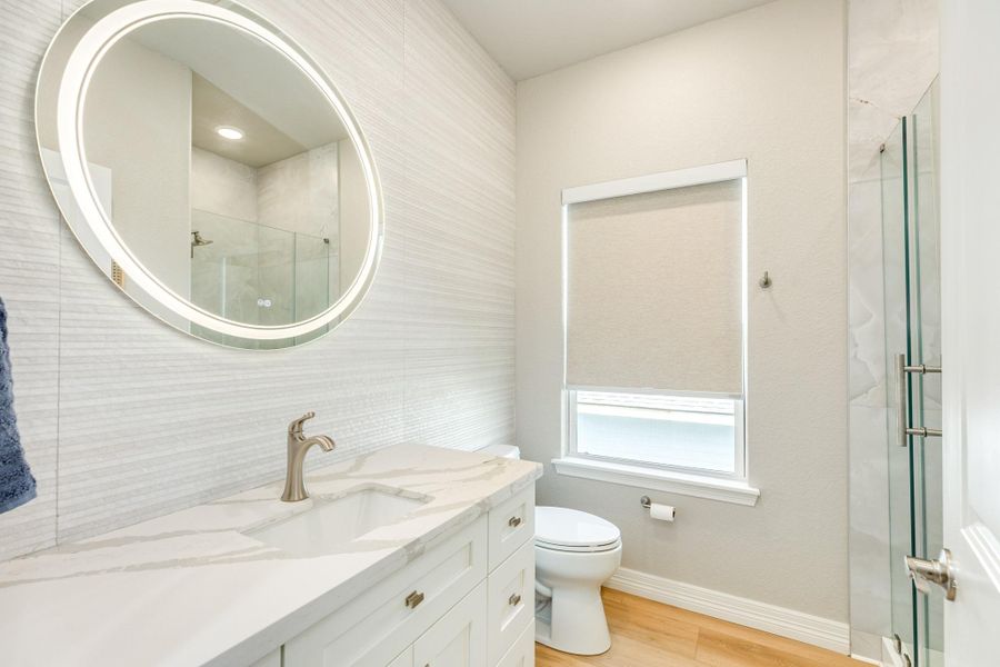 Modern guest bathroom showcases a quartz vanity, designer lighting, and a beautifully tiled walk-in glass shower.