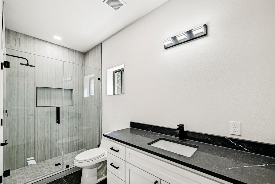 Bathroom with vanity, a shower stall, and dark tile patterned flooring