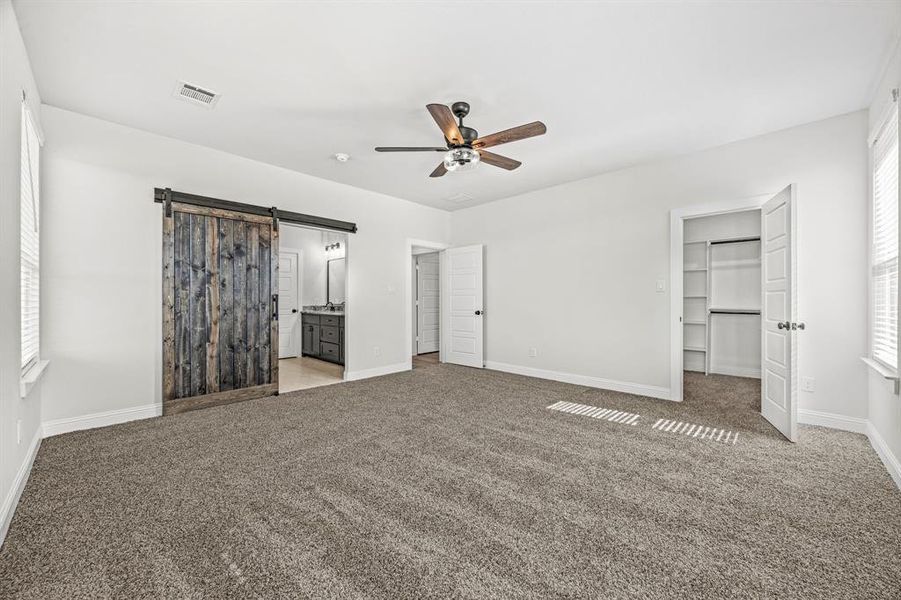 Unfurnished bedroom with a barn door, light carpet, ceiling fan, and ensuite bath