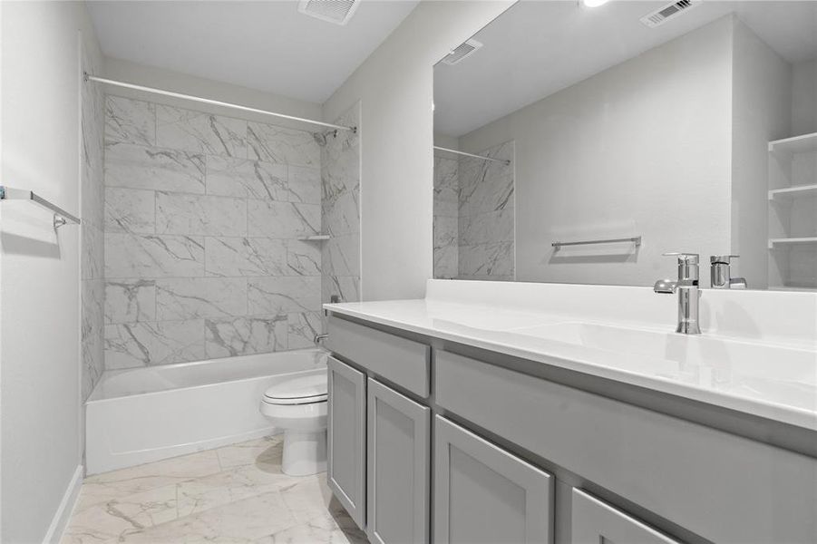 Secondary bath features tile flooring, bath/shower combo with tile surround, stained wood cabinets, beautiful light countertop, mirror, dark, sleek fixtures and modern finishes!