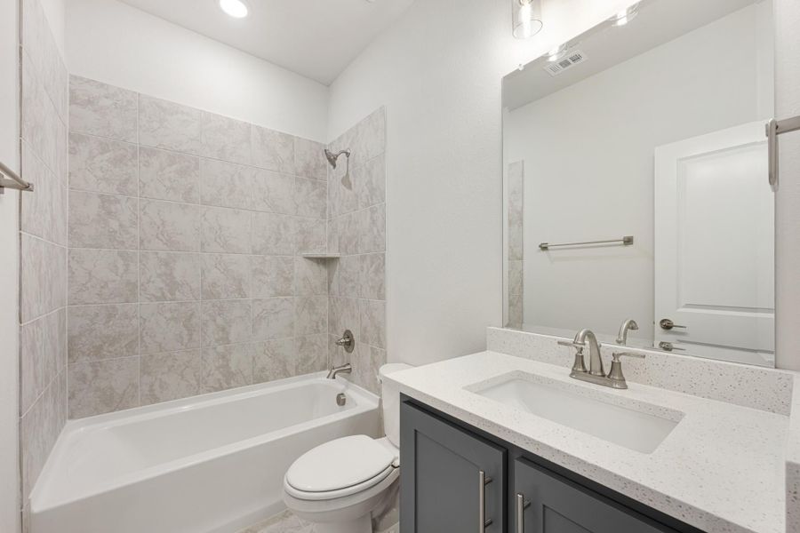 Bathroom with tiled tub-shower combo, gray vanity with quartz countertop, and large mirror Bathroom with tiled tub-shower combo, gray vanity with quartz countertop, and large mirror