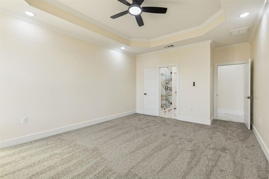 Unfurnished bedroom featuring a raised ceiling, ornamental molding, carpet, a ceiling fan, and connected bathroom