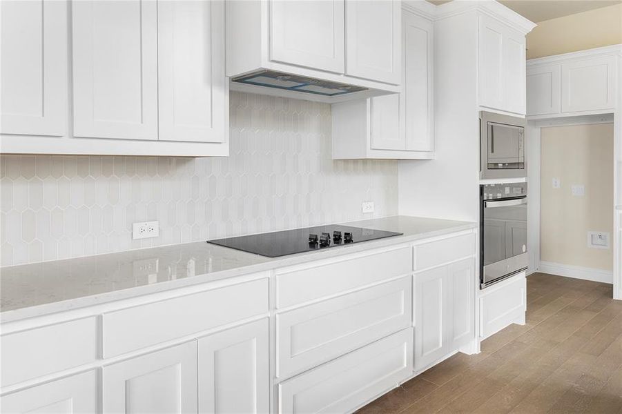 Kitchen featuring stainless steel oven, white cabinetry, premium range hood, black electric cooktop, and hardwood / wood-style flooring