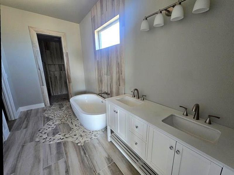 Bathroom with double vanity, wood finish floors, and a soaking tub