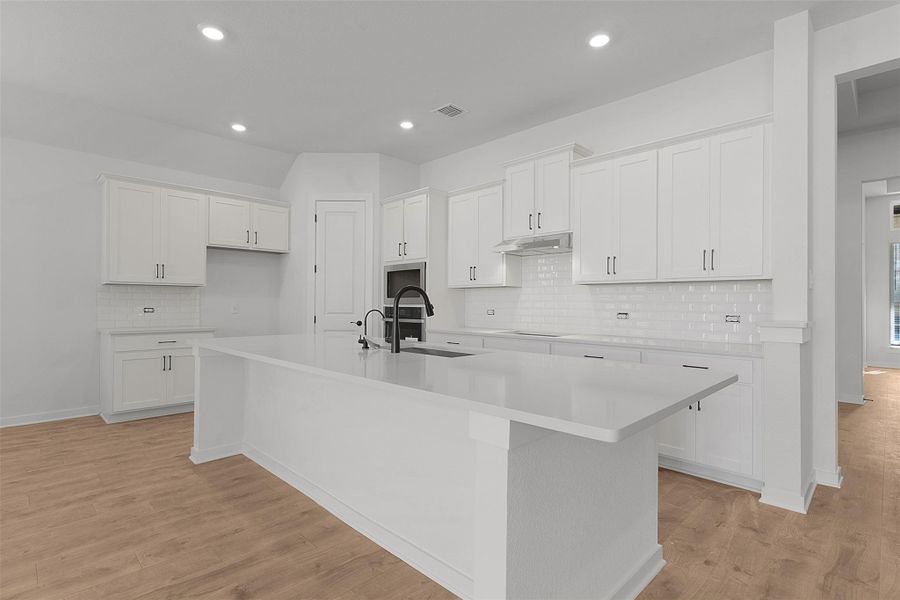 Kitchen with backsplash, white cabinetry, a kitchen island with sink, light wood finished floors, and recessed lighting