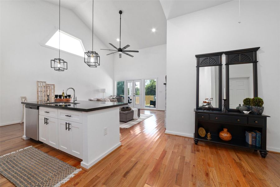 This is a bright, open-concept living space with hardwood floors, featuring a cozy living room, and a modern kitchen with white cabinetry and stainless steel appliances. Ceiling fans and pendant lights add a touch of elegance. This is a bright, open-concept living space with hardwood floors, featuring a cozy living room, and a modern kitchen with white cabinetry and stainless steel appliances. Ceiling fans and pendant lights add a touch of elegance.