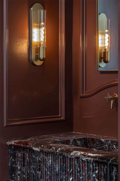 Softly lit powder room boasts expertly fabricated integrated marble sink, rich paneled walls and designer lighting. Softly lit powder room boasts expertly fabricated integrated marble sink, rich paneled walls and designer lighting.