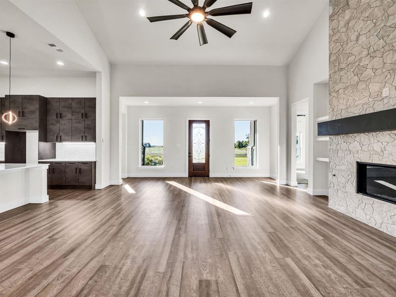 Unfurnished living room with a stone fireplace, hardwood / wood-style floors, ceiling fan, and vaulted ceiling