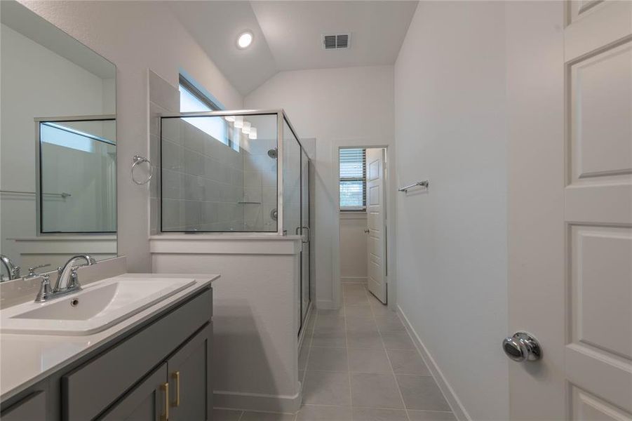 Bathroom featuring a shower stall, vanity, tile patterned flooring, healthy amount of natural light, and lofted ceiling