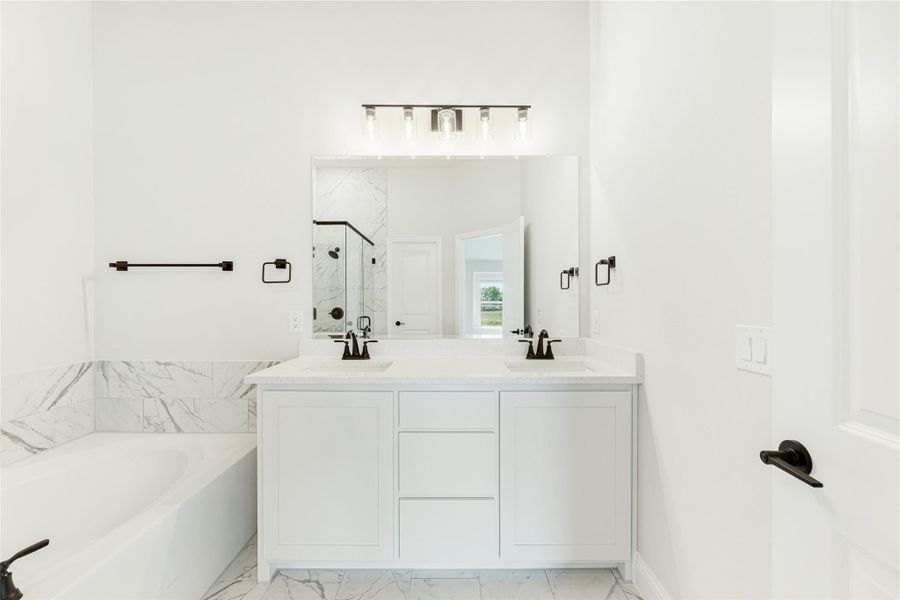 White bathroom with double sink vanity, large mirror, soaking tub, and marble tile floors
