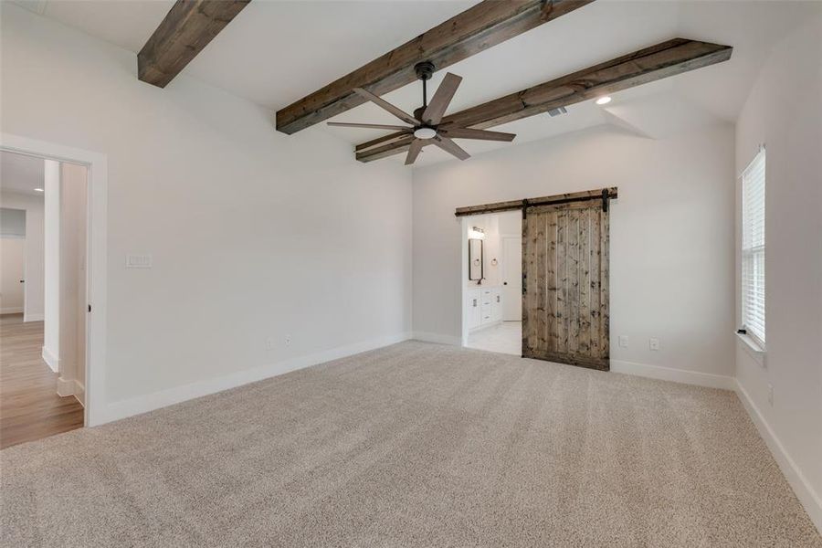 Carpeted spare room featuring a barn door, beam ceiling, and ceiling fan