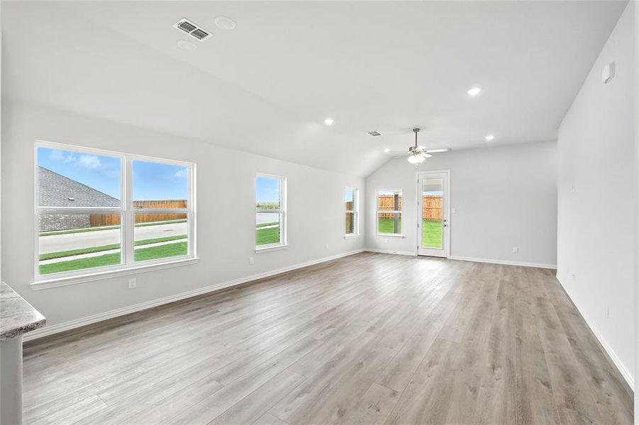 Unfurnished living room featuring healthy amount of natural light, light wood-type flooring, ceiling fan, vaulted ceiling, and recessed lighting Unfurnished living room featuring healthy amount of natural light, light wood-type flooring, ceiling fan, vaulted ceiling, and recessed lighting