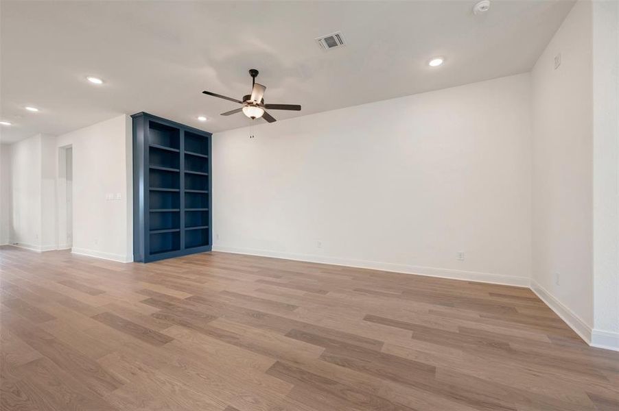 Spacious room featuring hardwood style flooring, a built-in bookshelf, a ceiling fan, and recessed lighting