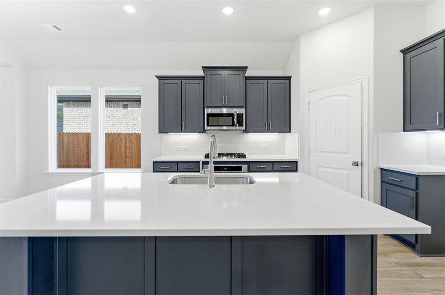 Kitchen featuring light stone counters, gray cabinets, an island with sink, light wood-type flooring, and recessed lighting