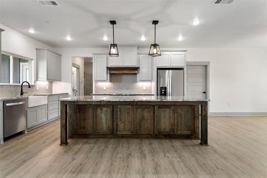 Kitchen with light stone counters, a center island, decorative light fixtures, and appliances with stainless steel finishes