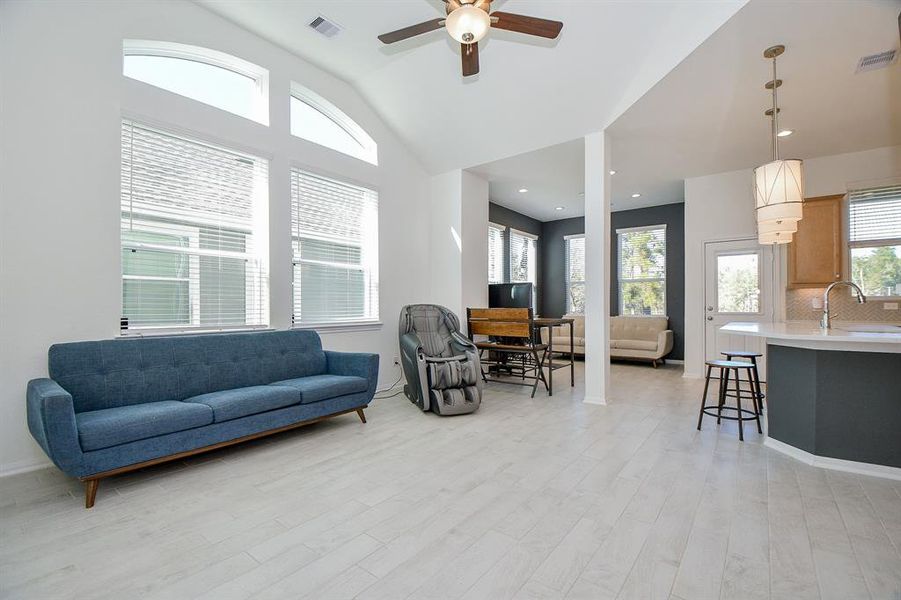 This inviting open floor plan offers the perfect blend of comfort and style. Thoughtfully designed with fresh neutral finishes, it features stunning wood-look tile flooring, a soft neutral palette, a sleek modern fireplace, and a soaring ceiling with chic lighting and a cooling fan. A striking wall of stacked windows bathes the space in natural light, creating a warm and welcoming ambiance.