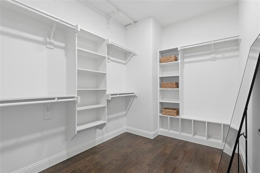 Walk-in closet featuring extensive built-in shelving, multiple hanging rods, and wood-finish flooring Walk-in closet featuring extensive built-in shelving, multiple hanging rods, and wood-finish flooring