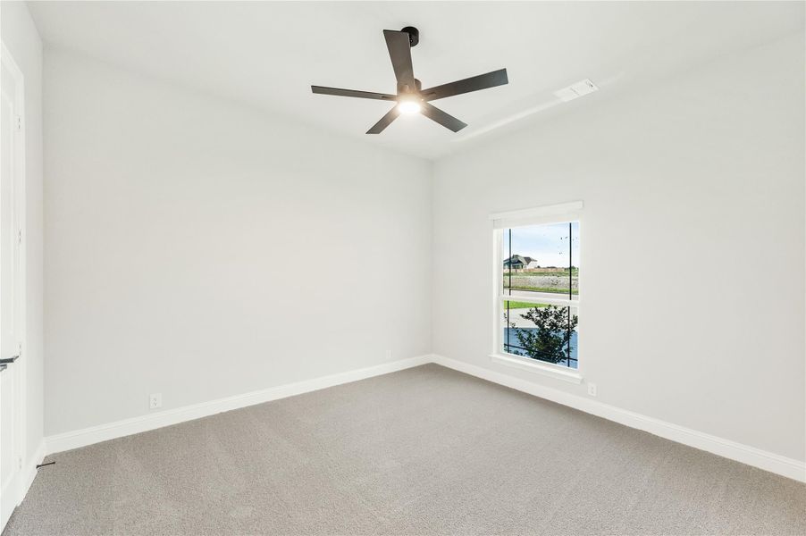 Empty bedroom with gray carpet, white walls, ceiling fan, and single window with outdoor view Empty bedroom with gray carpet, white walls, ceiling fan, and single window with outdoor view