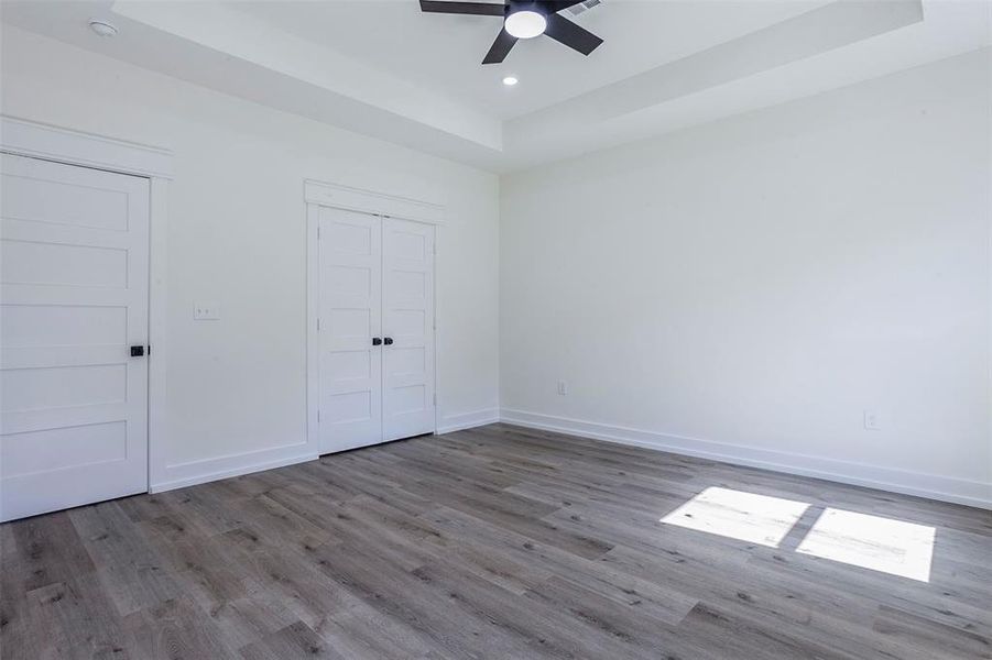 Spacious room featuring wood-finish flooring, white walls, and a tray ceiling with a built-in ceiling fan