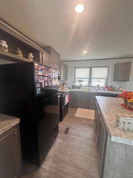 Kitchen with black appliances, light countertops, light wood-style floors, recessed lighting, and open shelves Kitchen with black appliances, light countertops, light wood-style floors, recessed lighting, and open shelves