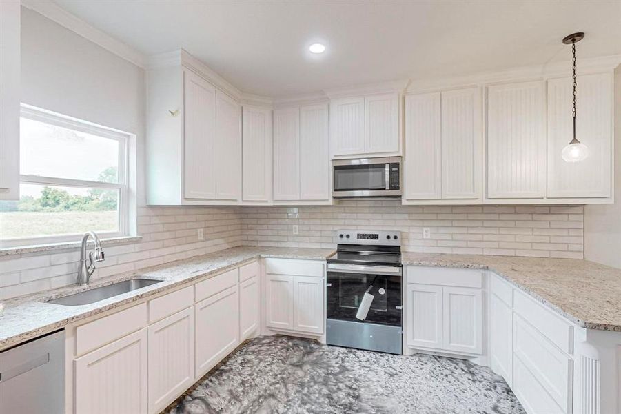 Kitchen featuring decorative backsplash, stainless steel appliances, sink, pendant lighting, and white cabinets